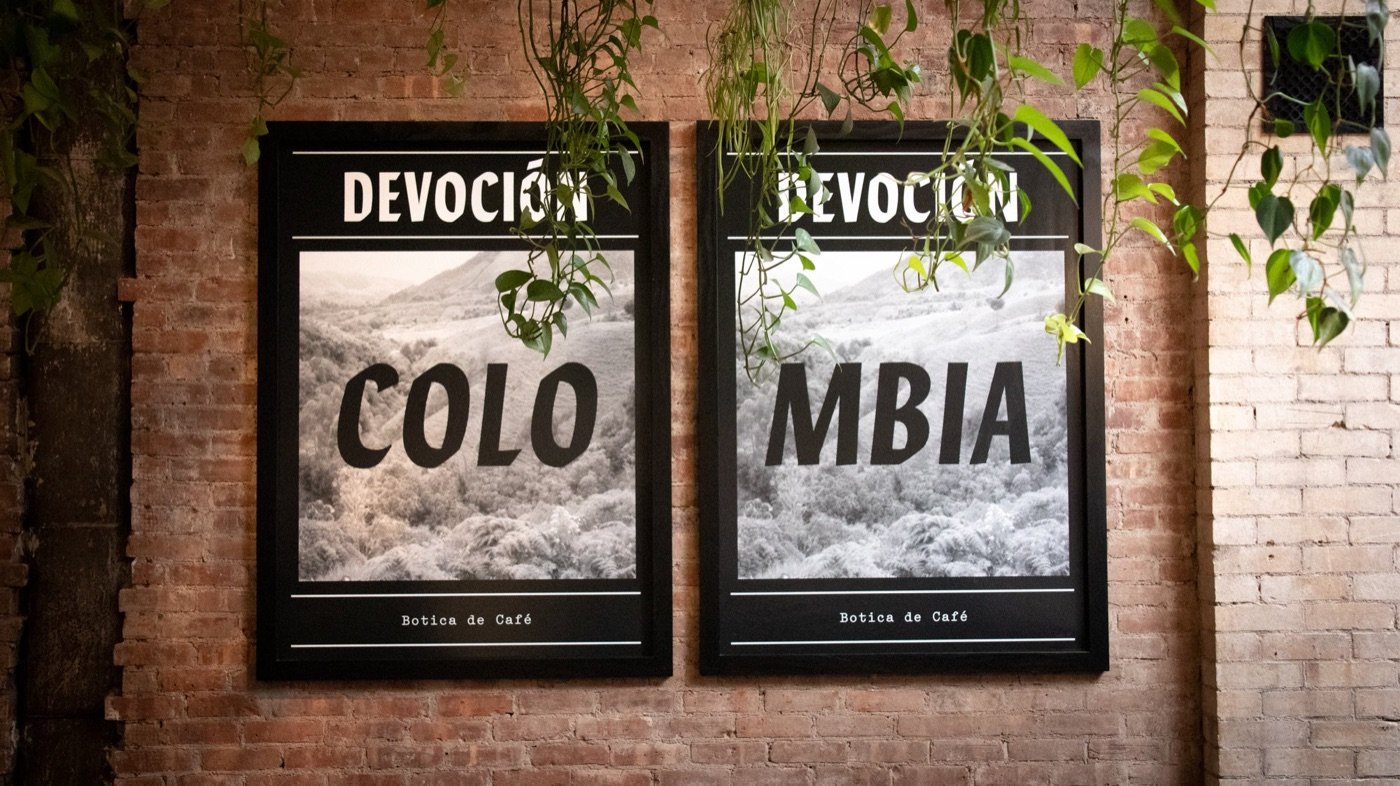 Framed Devoción Colombia artwork on a brick wall with hanging plants